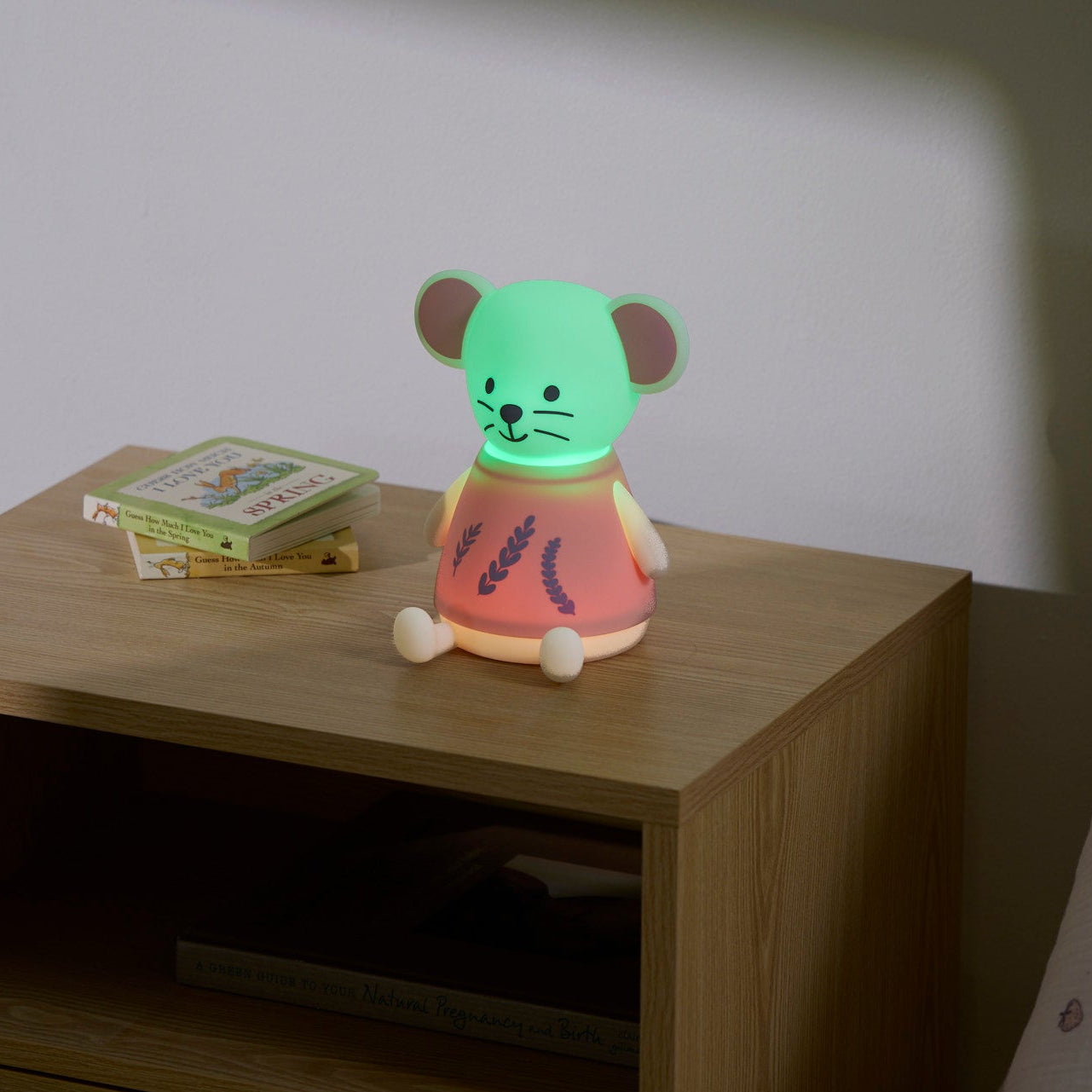 Children's night light shaped like a mouse on a wooden nightstand with a book in the background.