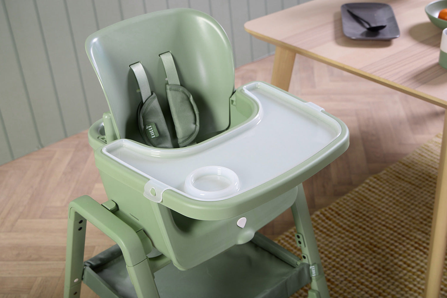 Nova Maison baby highchair in green on a wooden floor with a neutral background
