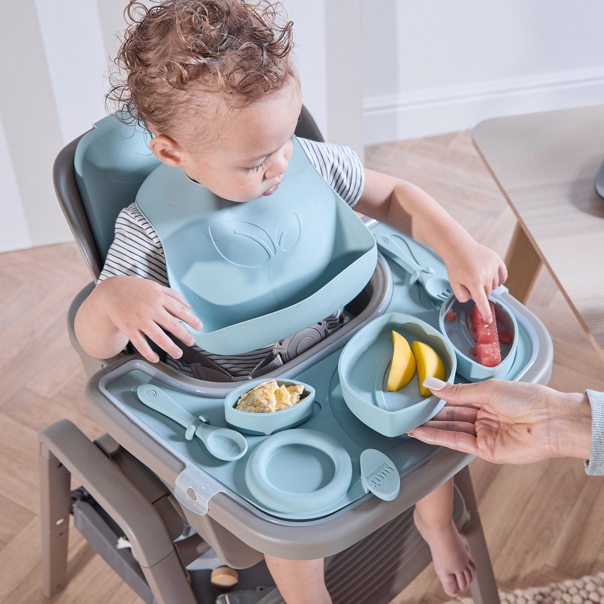 A child in the Nova Maison highchair with the accessory pack, eating fruit with a bib on.