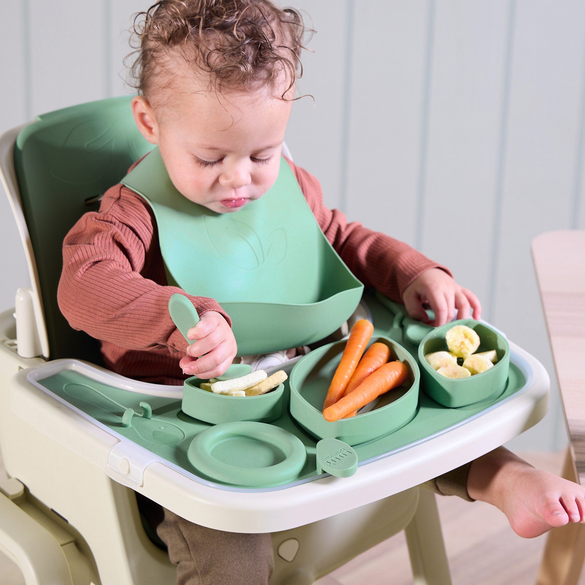 A baby sitting comfortably and eating in the Nova Maison highchair, with the green and white accessory pack showcased. A bright, lifestyle-focused image highlighting mealtime moments and the product’s stylish design.