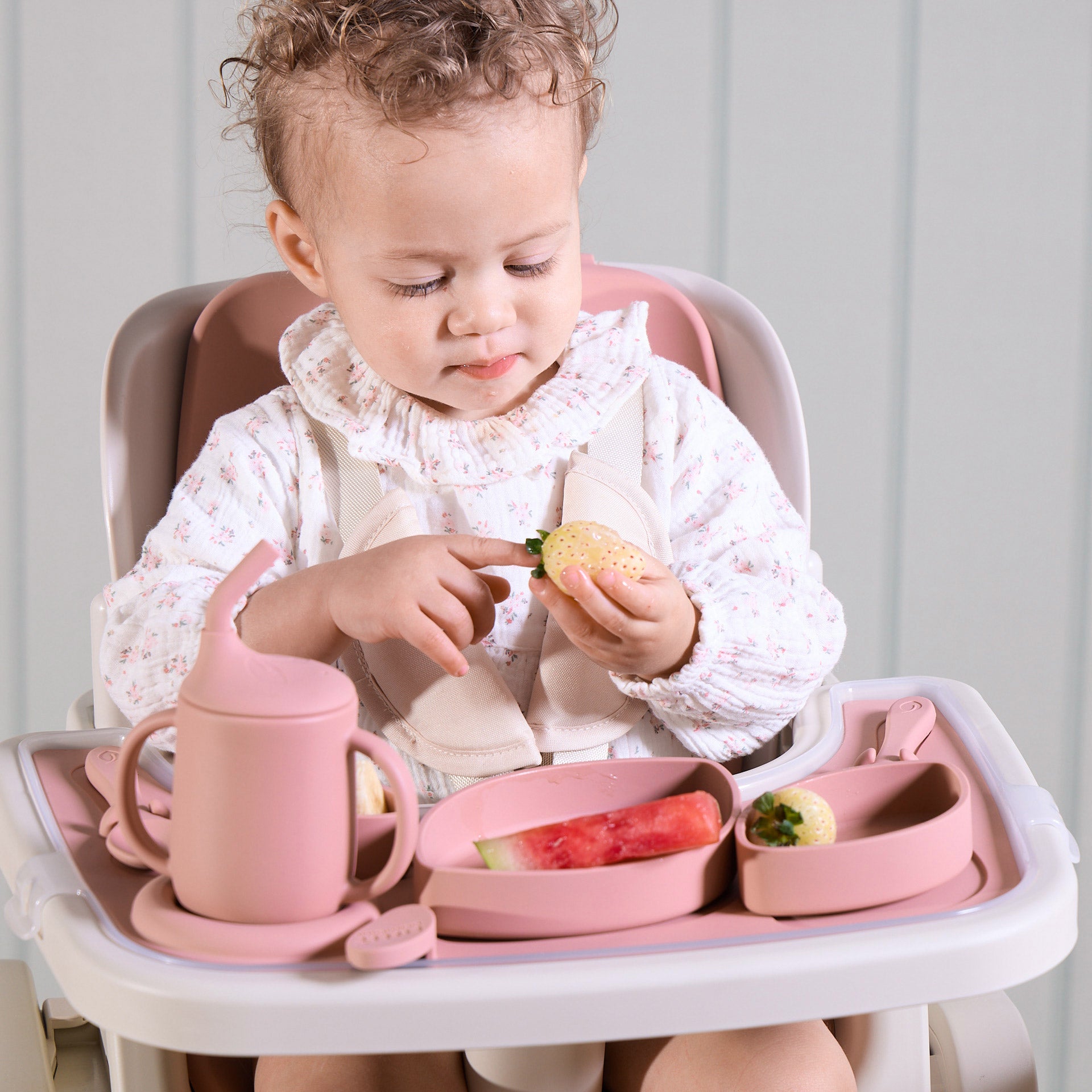 A child sitting in the Nova Maison highchair with pink tableware set and food