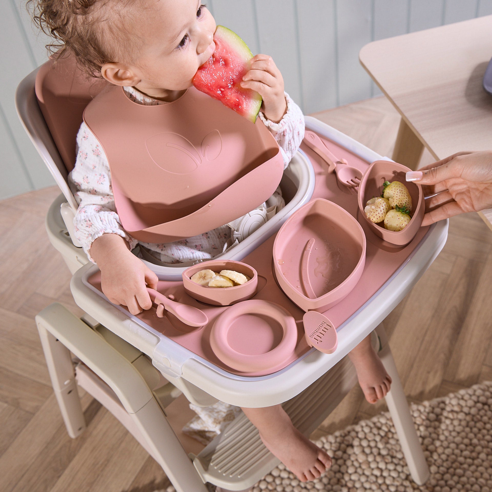 A baby eating food seating on the Nova Maison highchair with the Nova accessory pack in pink