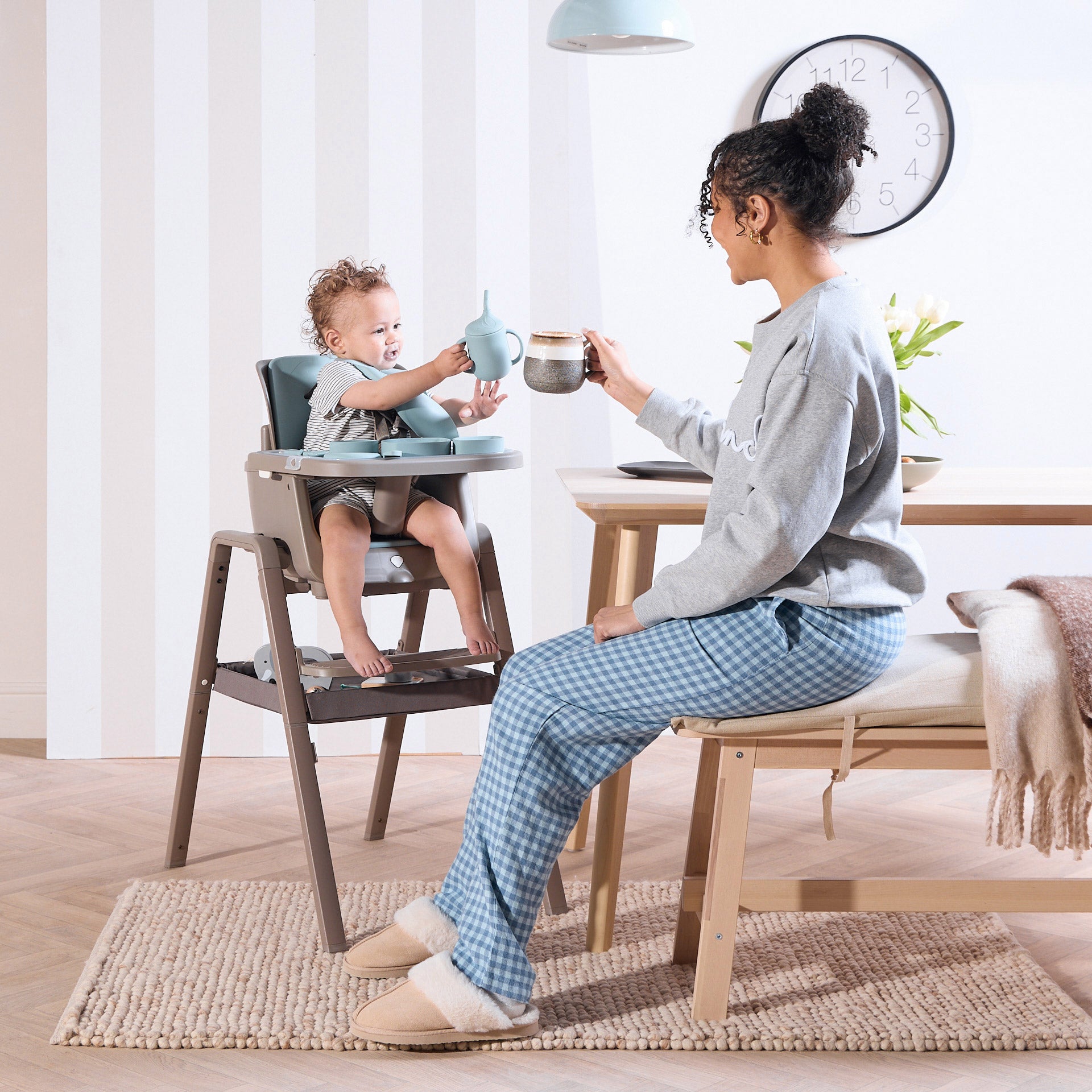 A woman and a child sitting in a dinning area holding a sippy cup.