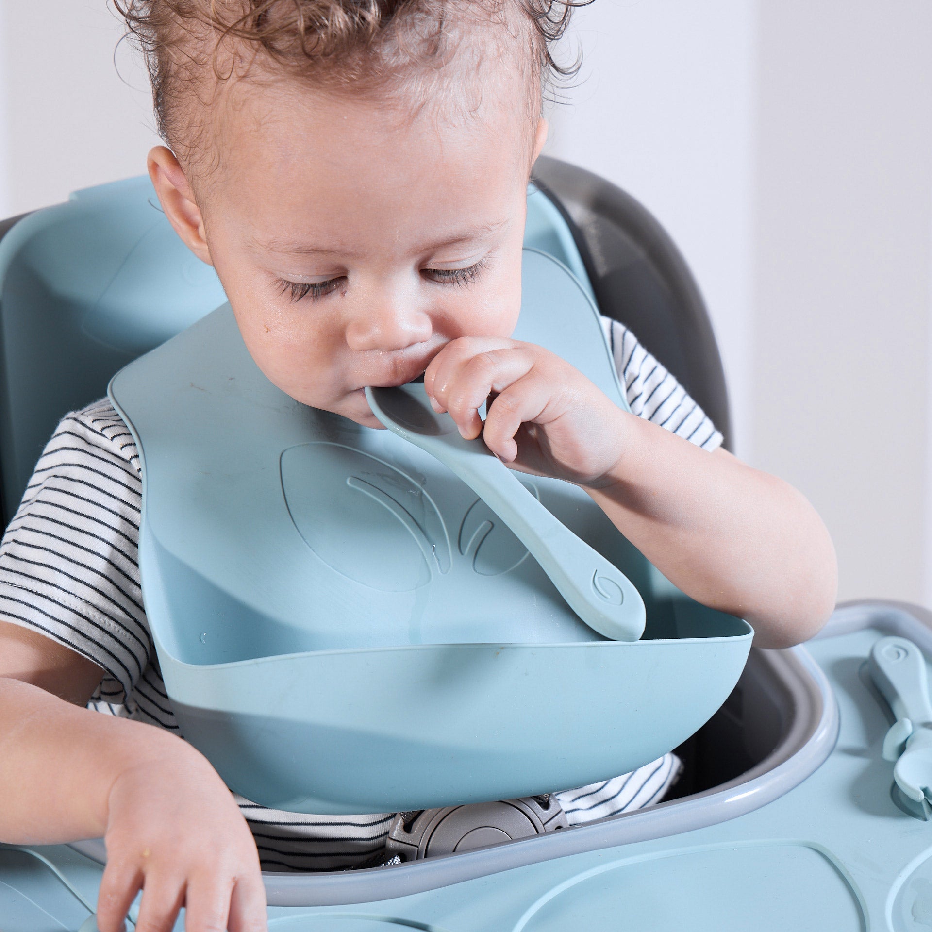 Child using the blue bib and spoon of the Nova accessory pack