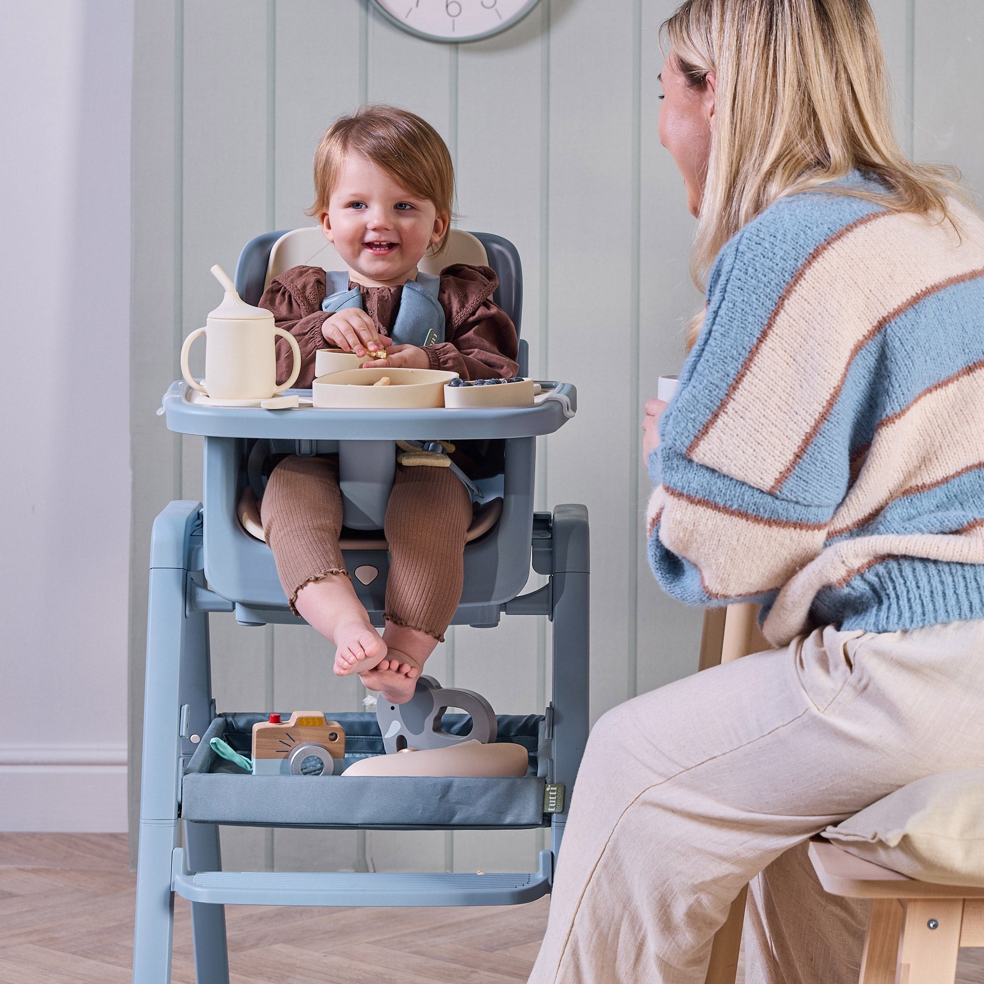 A child sitting on the Nova Maison highchair with the accessory pack smilling to her mother.