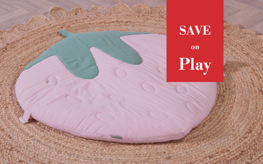 A strawberry-shaped play mat in light pink with a mint green leaf top, placed on a woven rug. A red promotional overlay on the right reads 'SAVE on Play'.