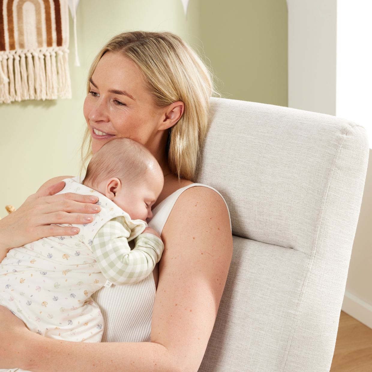 A woman holding a baby in a chair with a neutral background