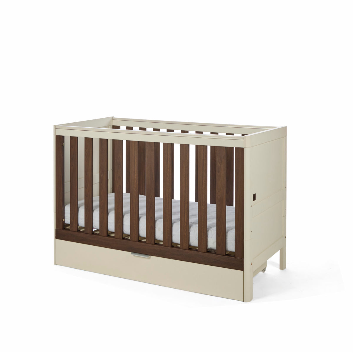 An angle view of the Riley cot bed in cashmere and rich walnut, featuring a drawer beneath it in a white background.