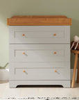 Rio chest changer in dove grey with oak top shown in nursery setting, offering three spacious drawers and warm two-tone finish