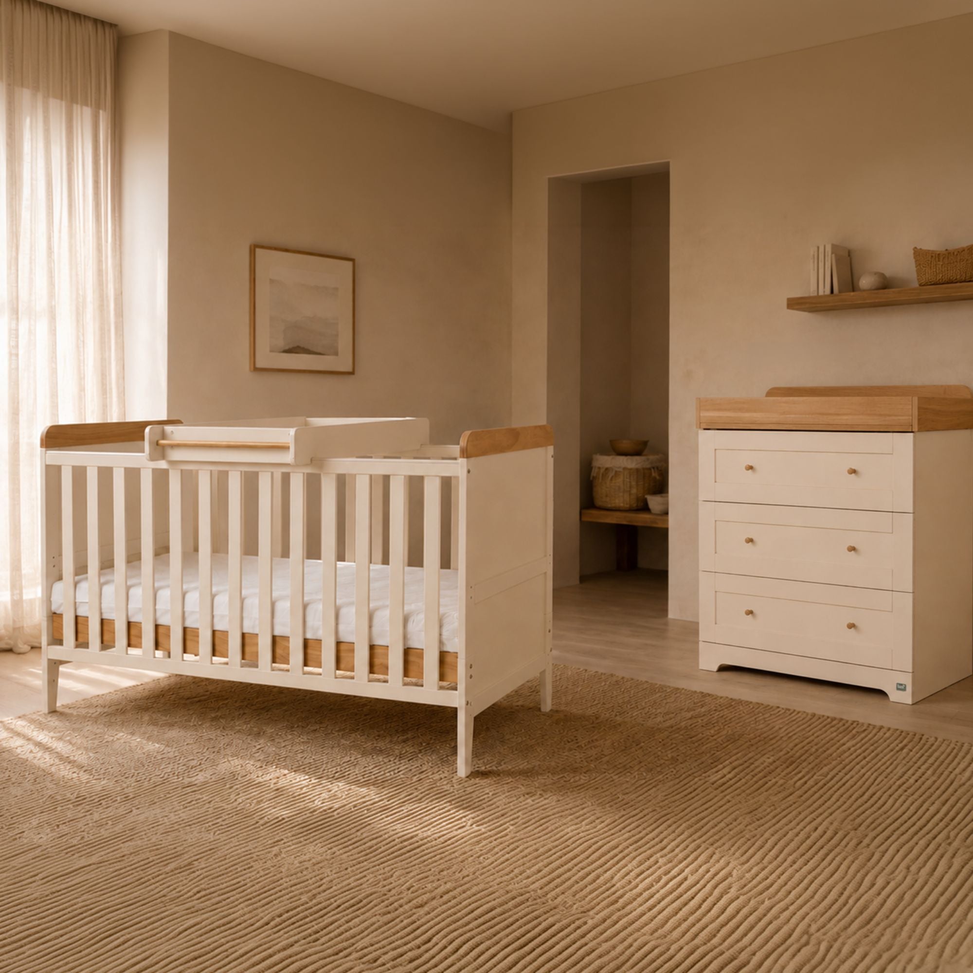 Rio baby cot bed in cashmere and oak, shown in a softly lit nursery next to a matching chest changer with a wood top.