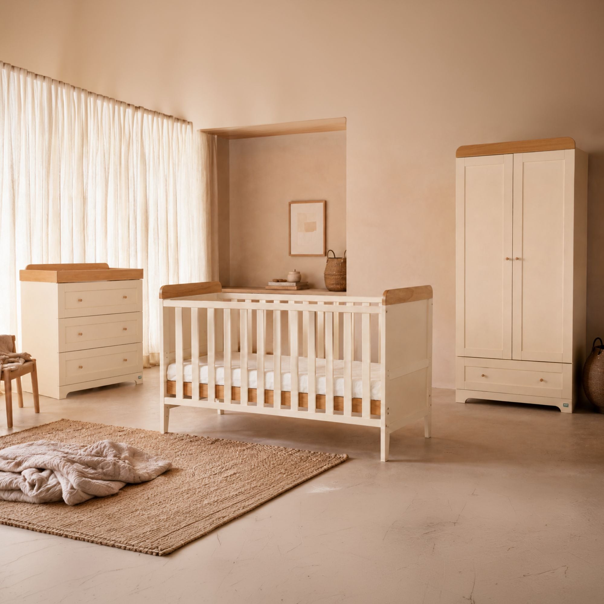 A coordinated nursery furniture set in a warm neutral room, including a cot bed, cot top changing, chest of drawers, and tall wardrobe, styled with a woven rug and soft textiles.
