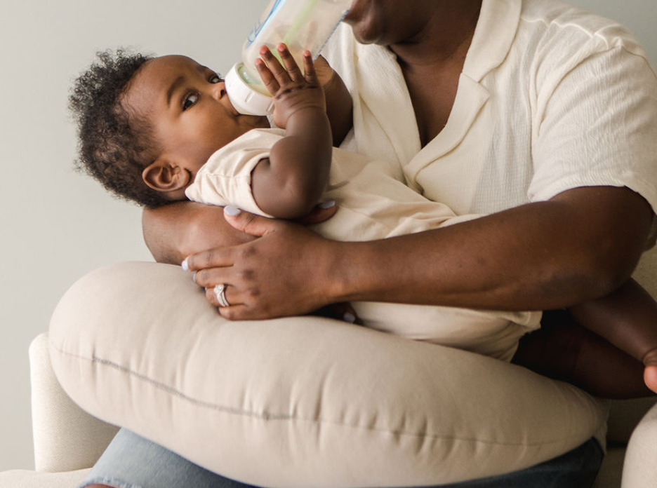 Parent bottle feeding baby using a nursing pillow for arm and back support