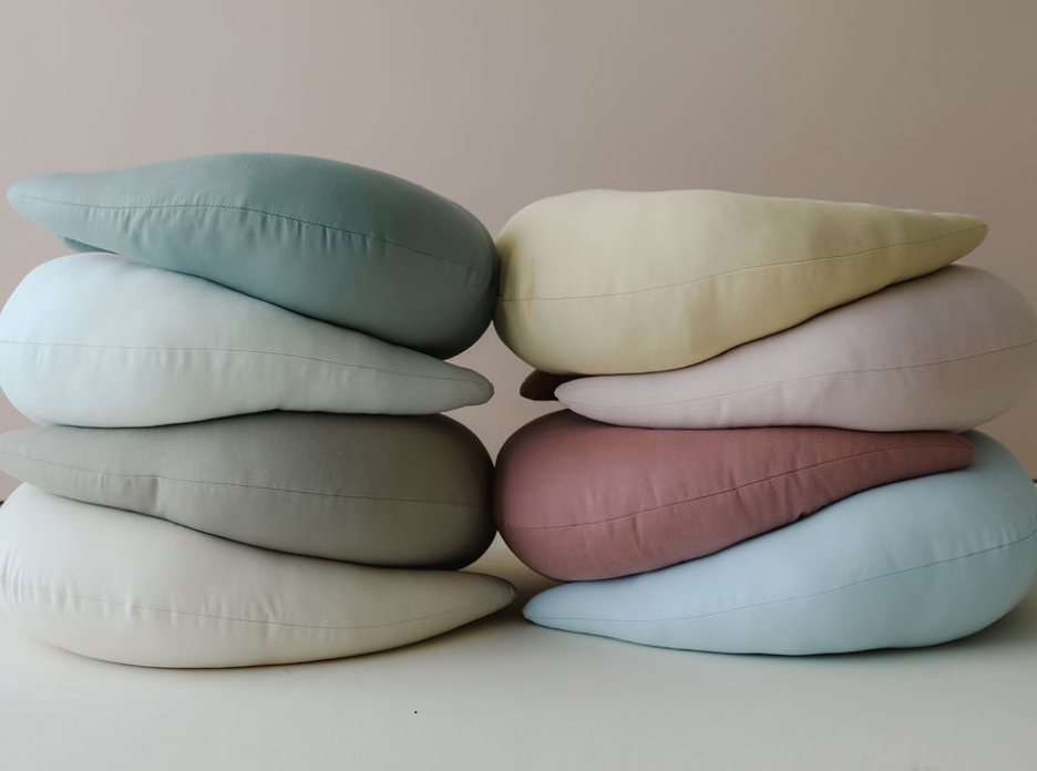Stack of eight teardrop-shaped nursing pillows in soft pastel shades