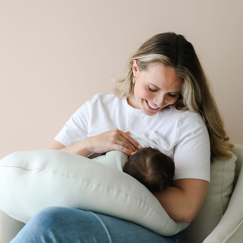 Smiling mother using the SMO nursing pillow in sage for comfortable breastfeeding