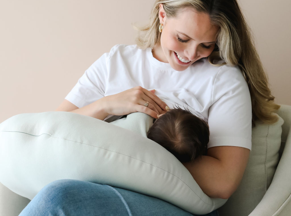Smiling mother breastfeeding with  nursing pillow in a supportive position