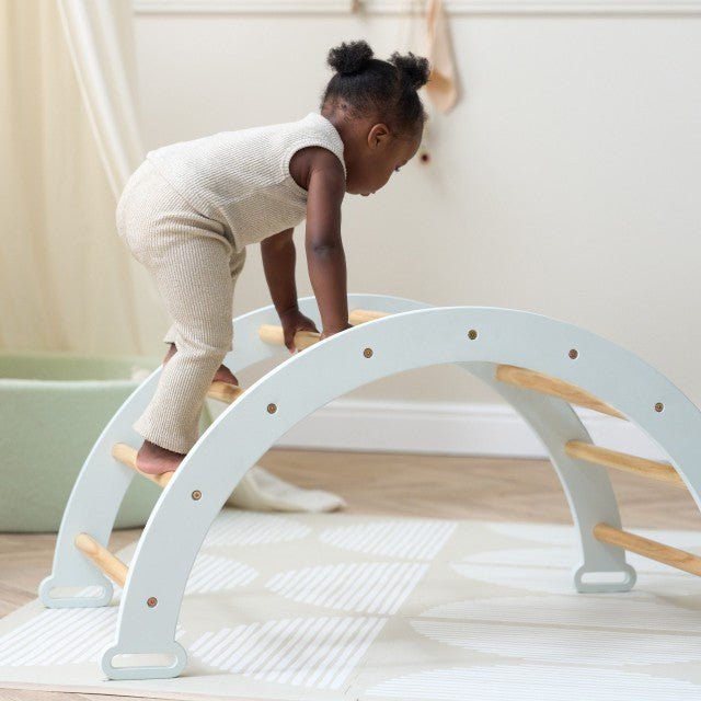 Girl playing on the Scala Arch in soft blue. Play arch designed for climbing, balance, and imaginative play.