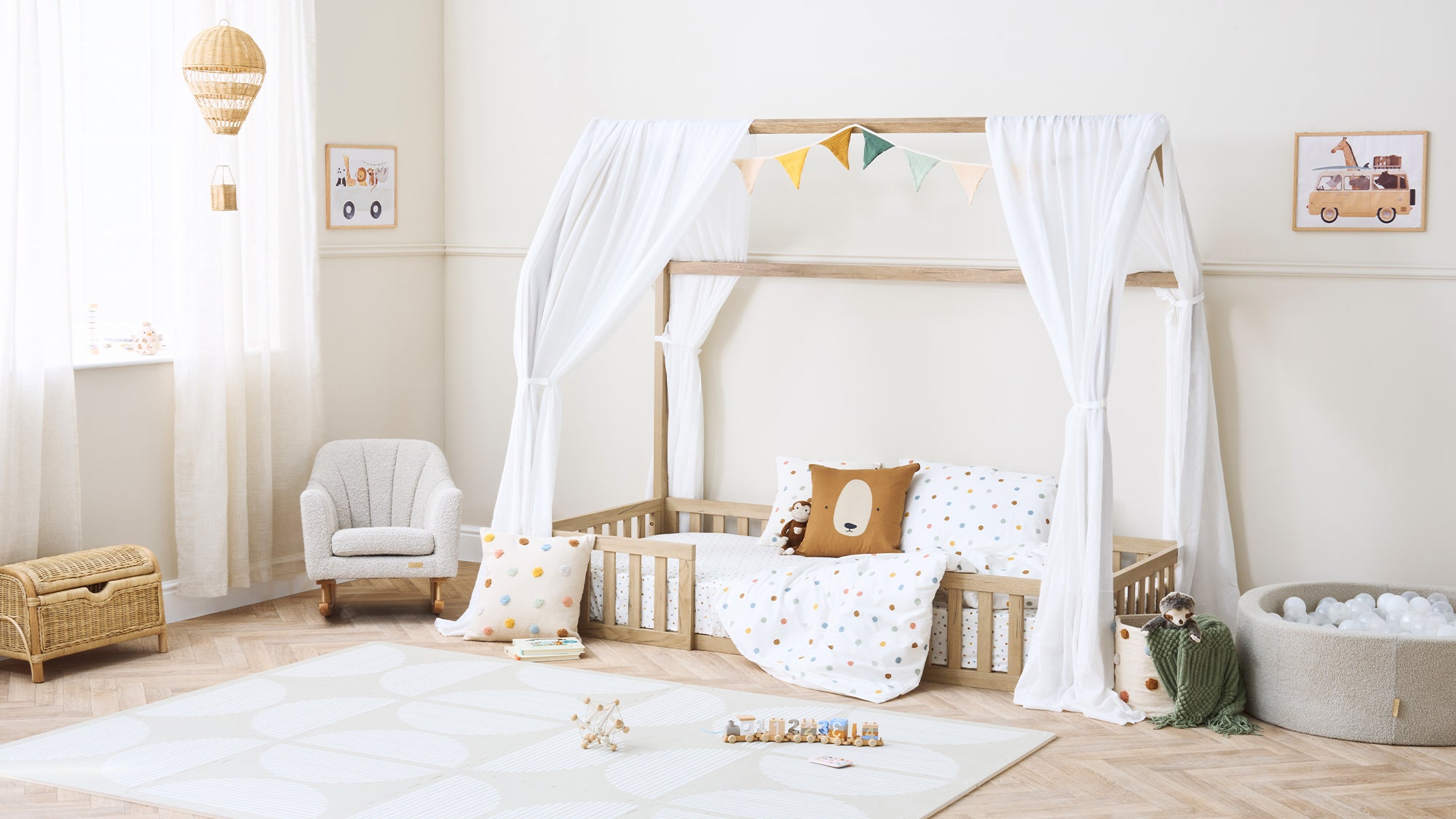 Calm, neutral nursery featuring a low canopy toddler bed, soft furnishings and play accessories styled in a light, airy space.