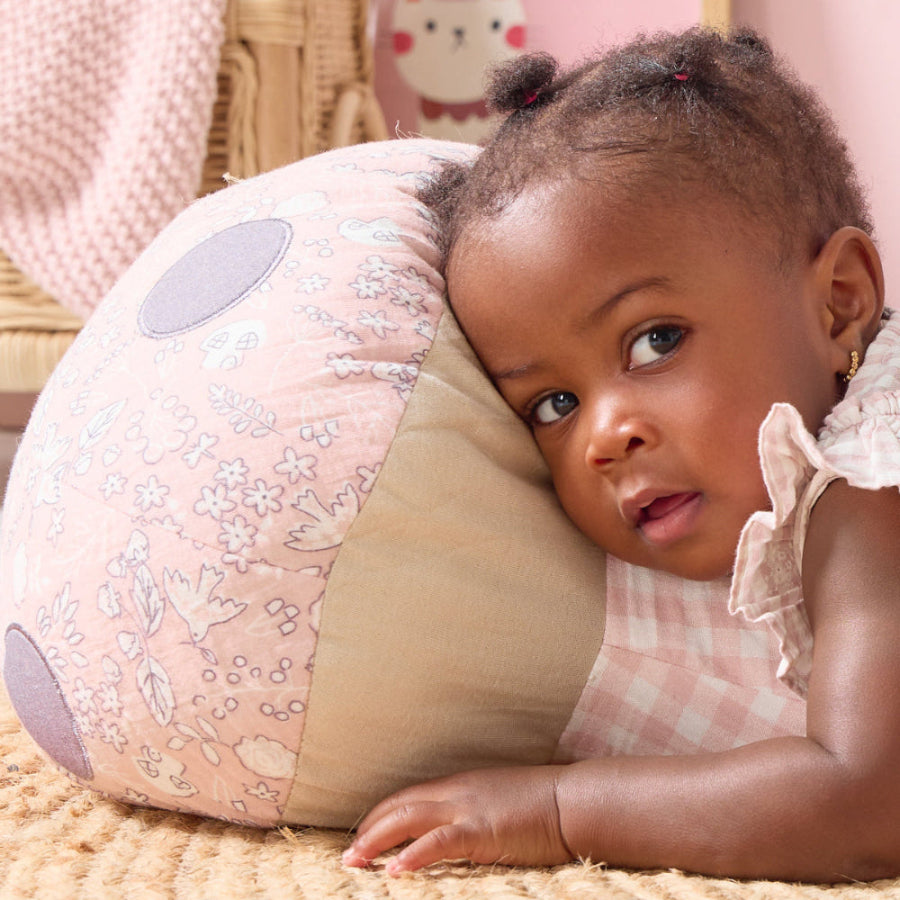 Toddler resting on the Soft Muslin Mushroom Cushion, showing its quilted floral print top and soft checked muslin base for comfort