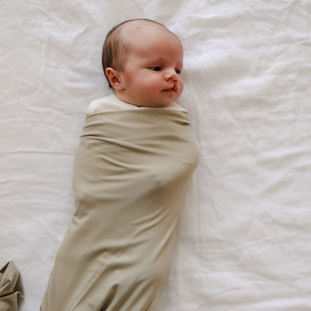 Newborn baby wrapped in a beige swaddle on a white blanket