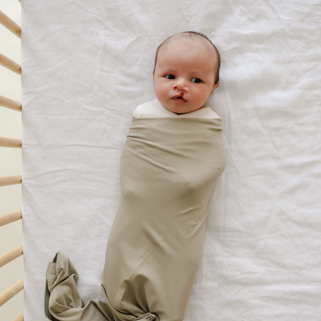 Newborn baby swaddled in a beige blanket on a white crib
