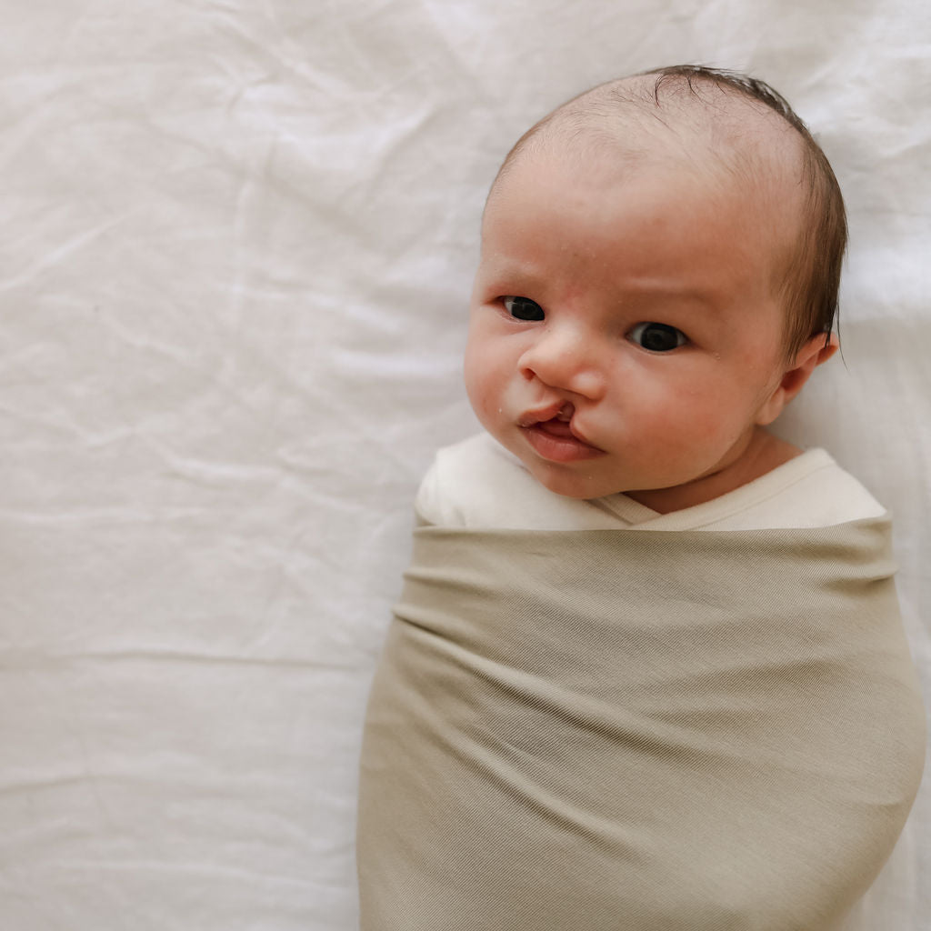 Newborn baby wrapped in a beige blanket on a white background