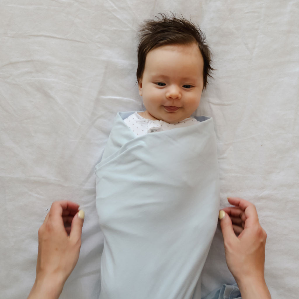 Baby swaddled in a light blue blanket on a white bed