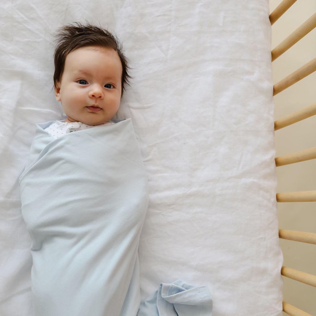 Baby swaddled in a light blue blanket lying on a white surface.