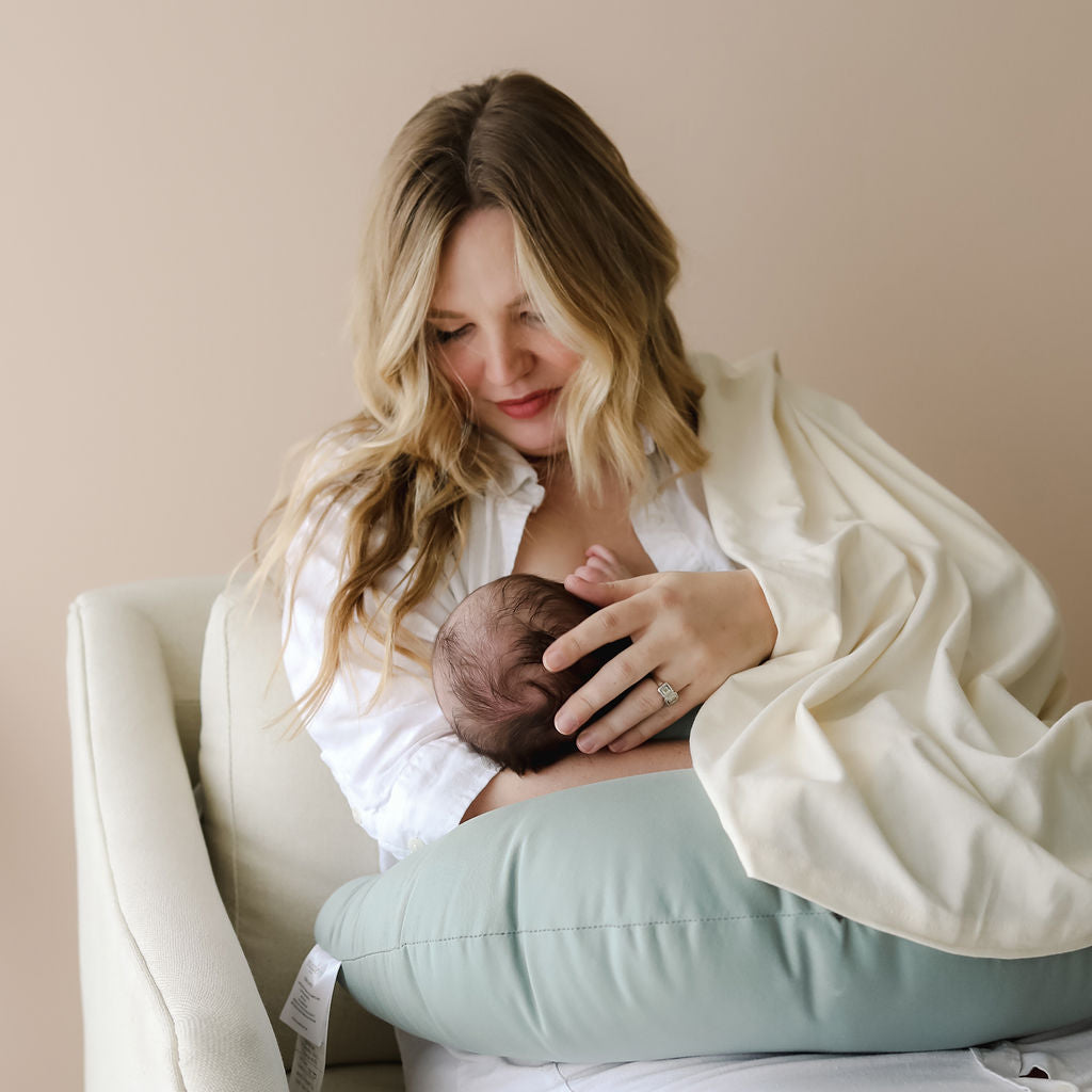 Woman breastfeeding a baby on a light blue cushion with a neutral background