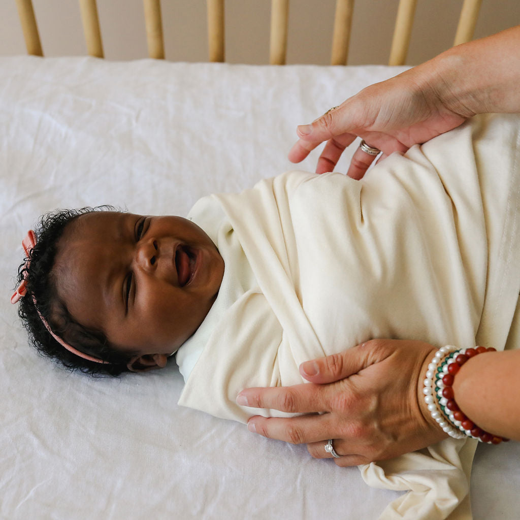 Newborn baby wrapped in a white blanket being held by an adult on a bed.