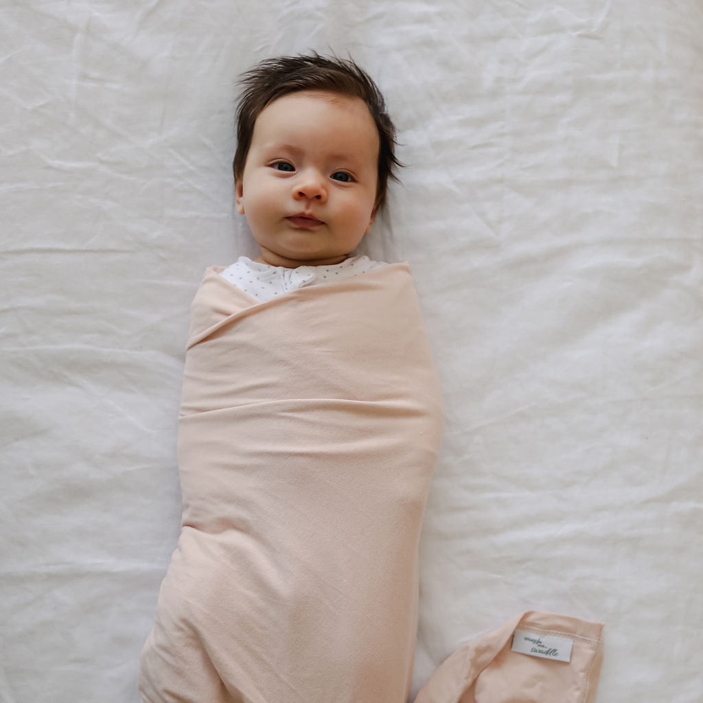 Newborn baby swaddled in a pink blanket on a white bed