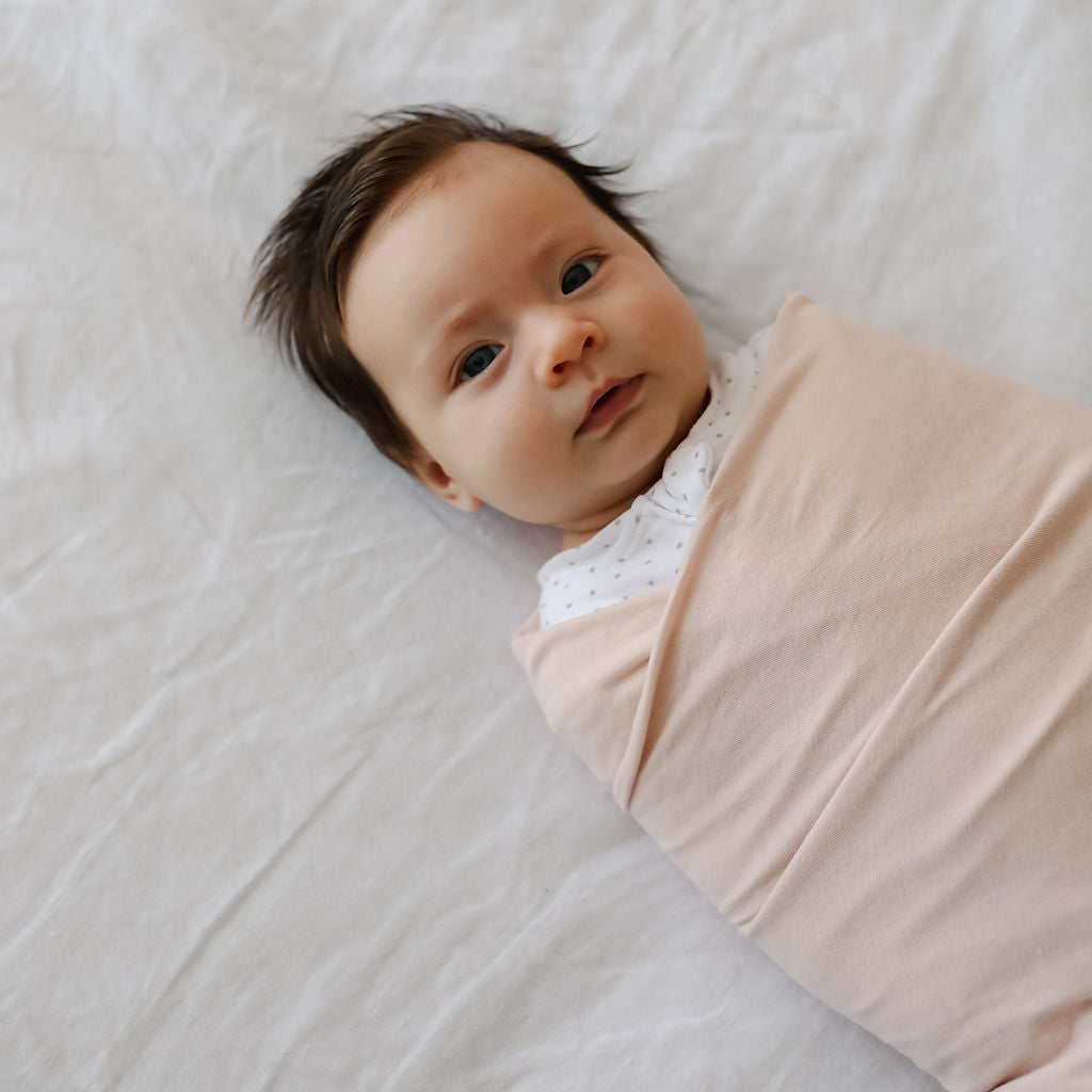 Newborn baby wrapped in a pink blanket on a light gray surface