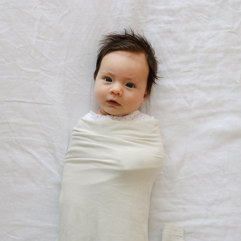 Baby swaddled in light green fabric on a white blanket