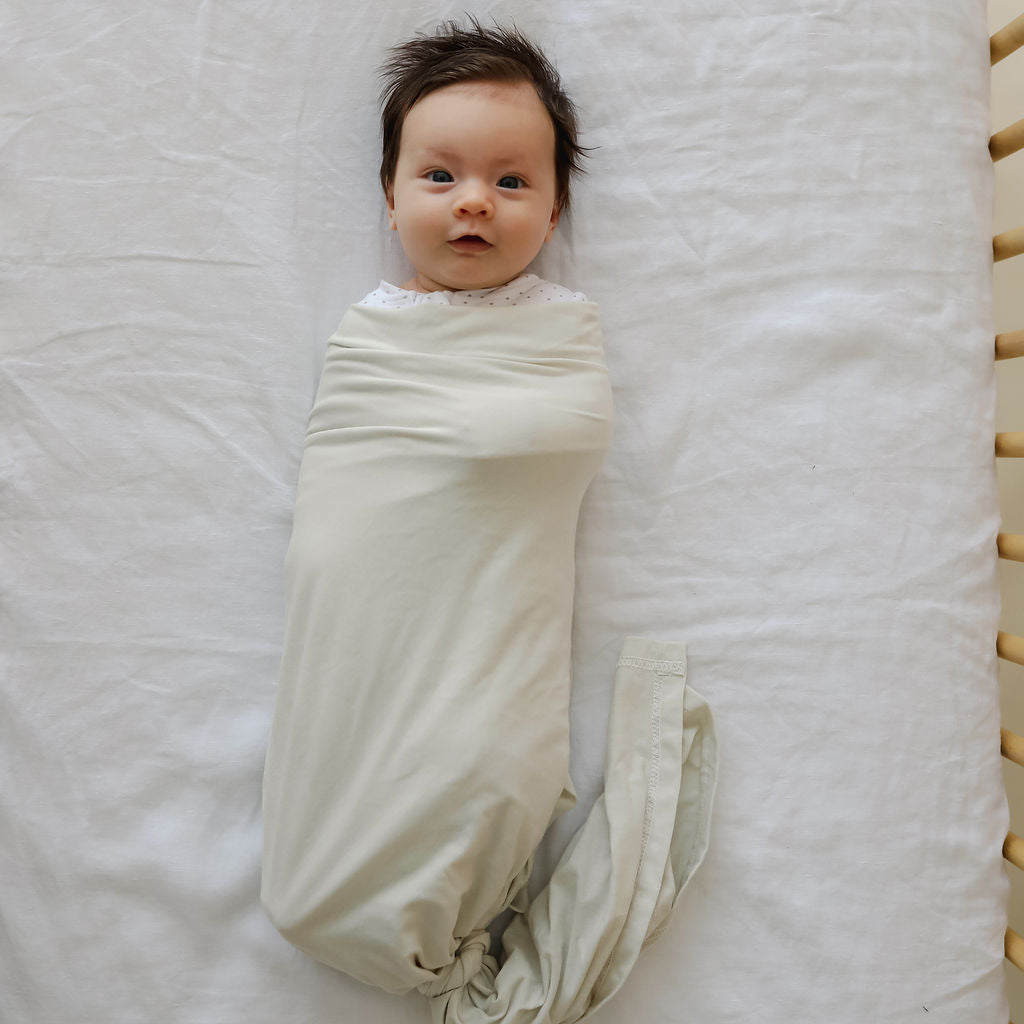 Newborn baby swaddled in a light green blanket on a textured surface