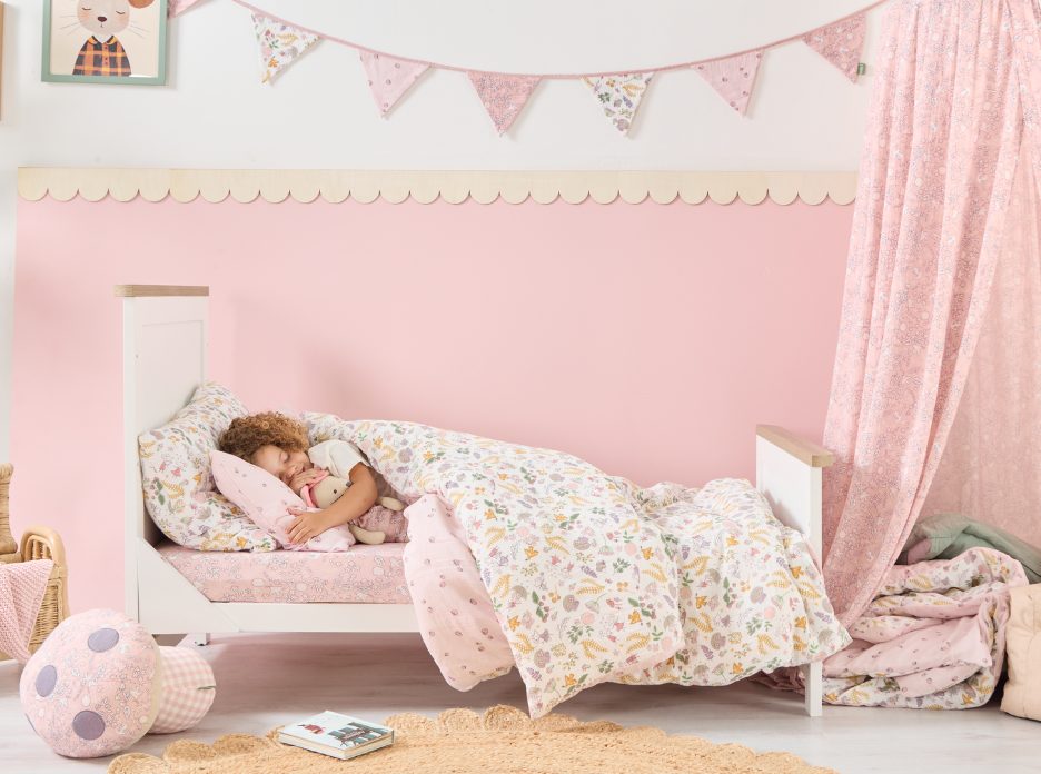 Child sleeping in a pink bed with floral bedding from the Tiny Tales collection, surrounded by decorative nursery elements.
