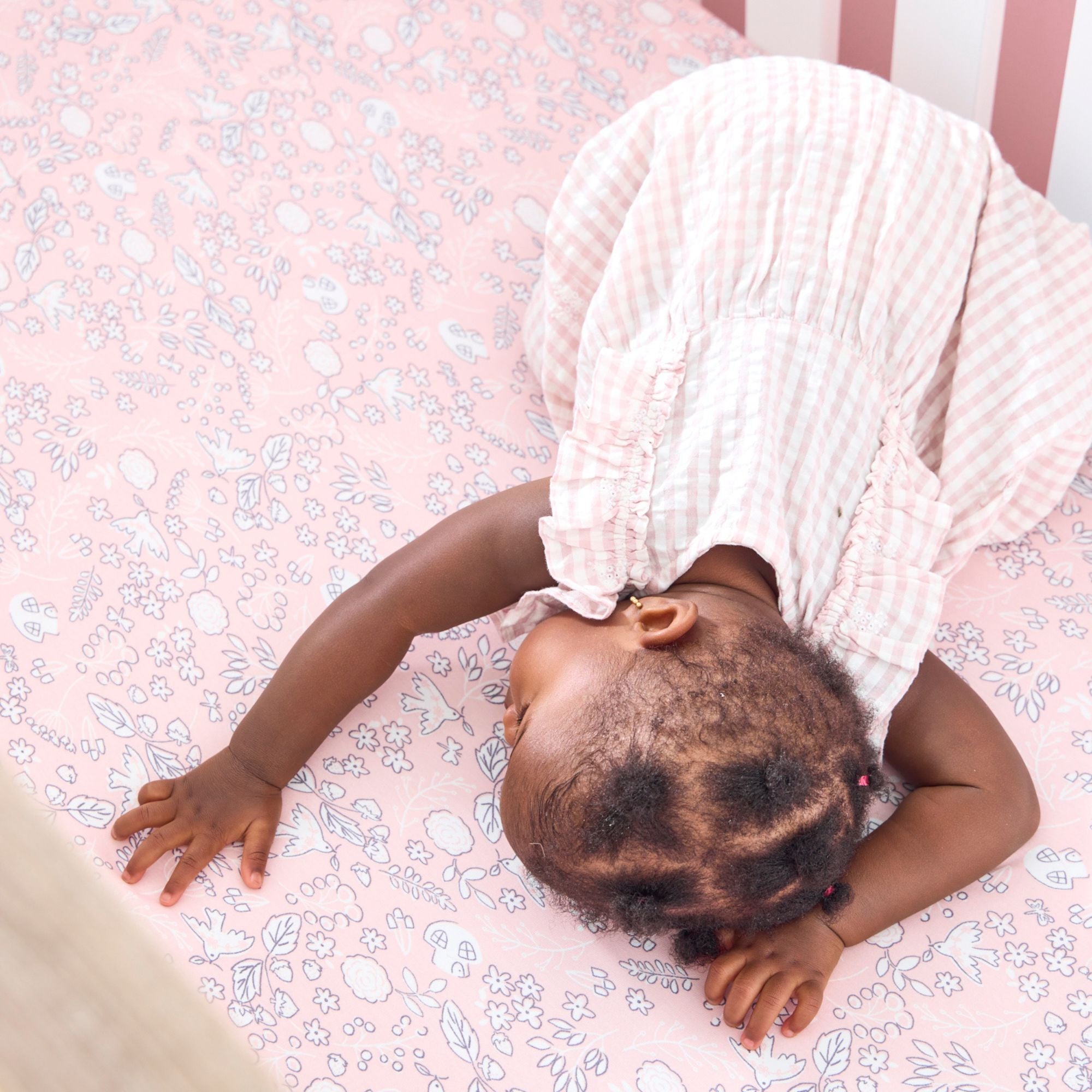 Baby lying on a pink floral cot bed fitted sheet from the Tiny Tails collection.