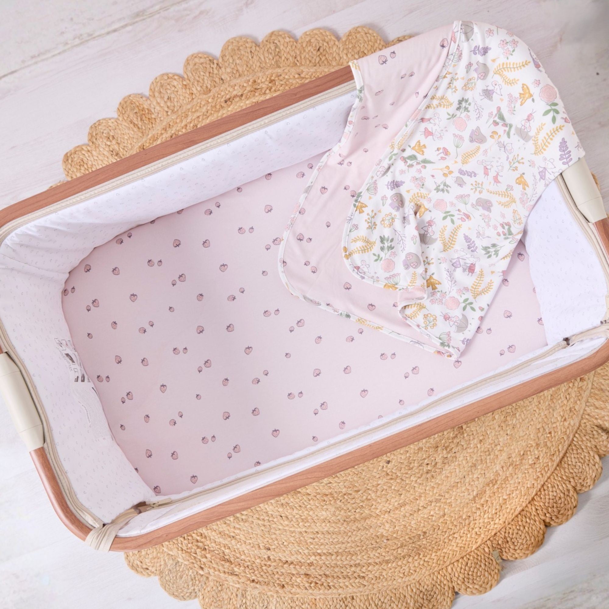 Baby crib with pink crib sheet and floral blanket on a light wooden floor.