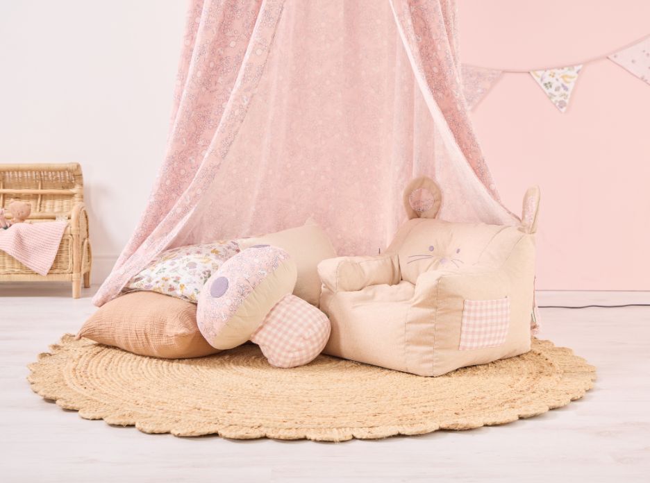 Tiny Tails pink nursery canopy styled as a cosy floor den with layered cushions and soft bunny armchair on a woven rug.