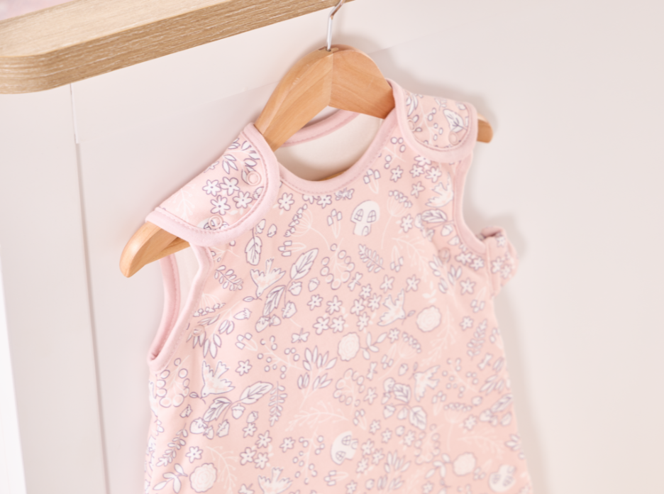 Close-up of the snap fastenings on the baby sleep bag from the Tiny Tales collection with a floral pattern, shown on a wooden hanger against a white background.