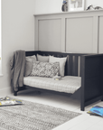 Tivoli cot bed in navy shown as a sofa bed with slatted back and panelled sides, styled with soft cushions in a modern nursery room.