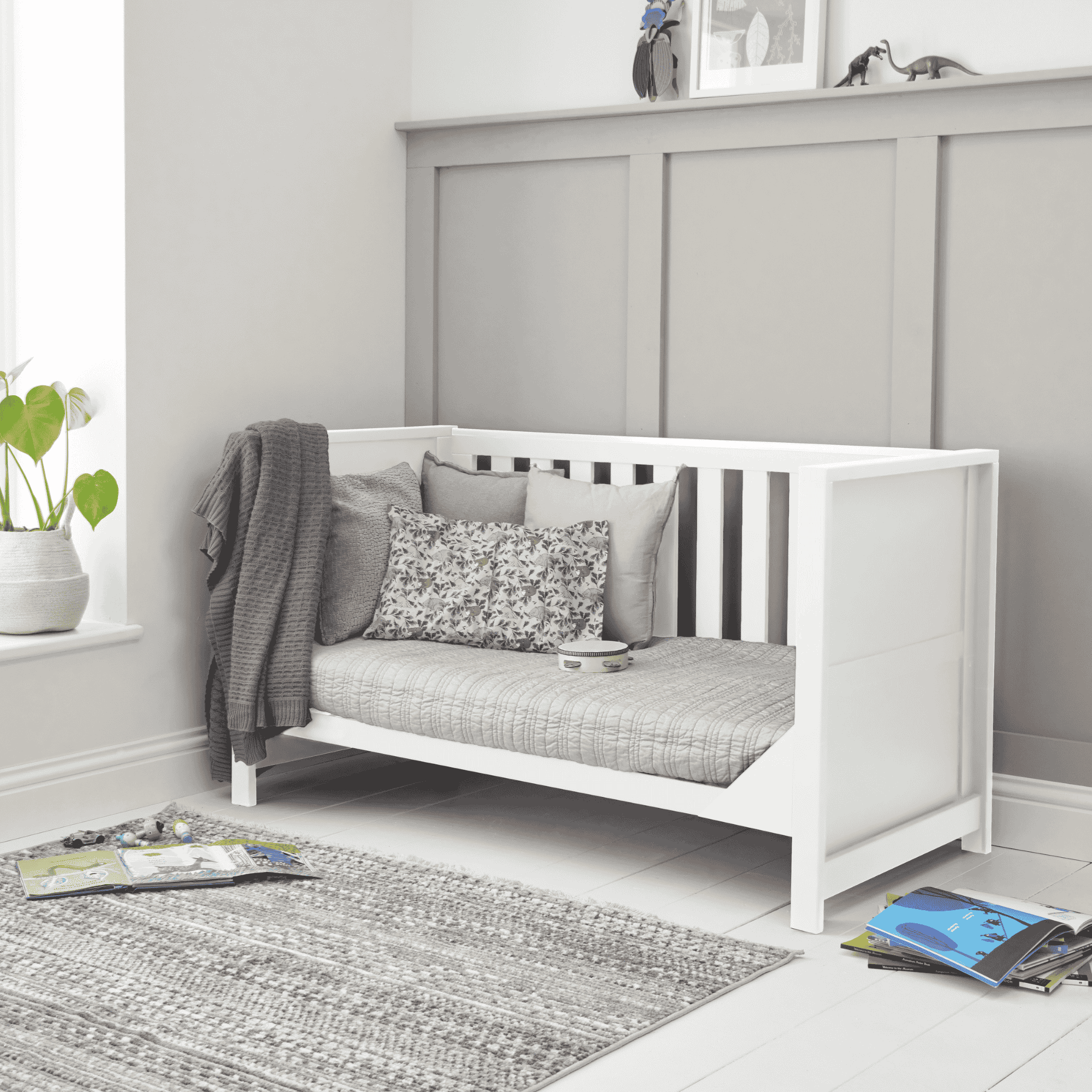 Tivoli cot bed in white styled as a sofa bed, featuring panelled sides, slatted back and cushioned seating in a calm nursery setting.