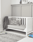 Tivoli cot bed in white styled as a sofa bed, featuring panelled sides, slatted back and cushioned seating in a calm nursery setting.