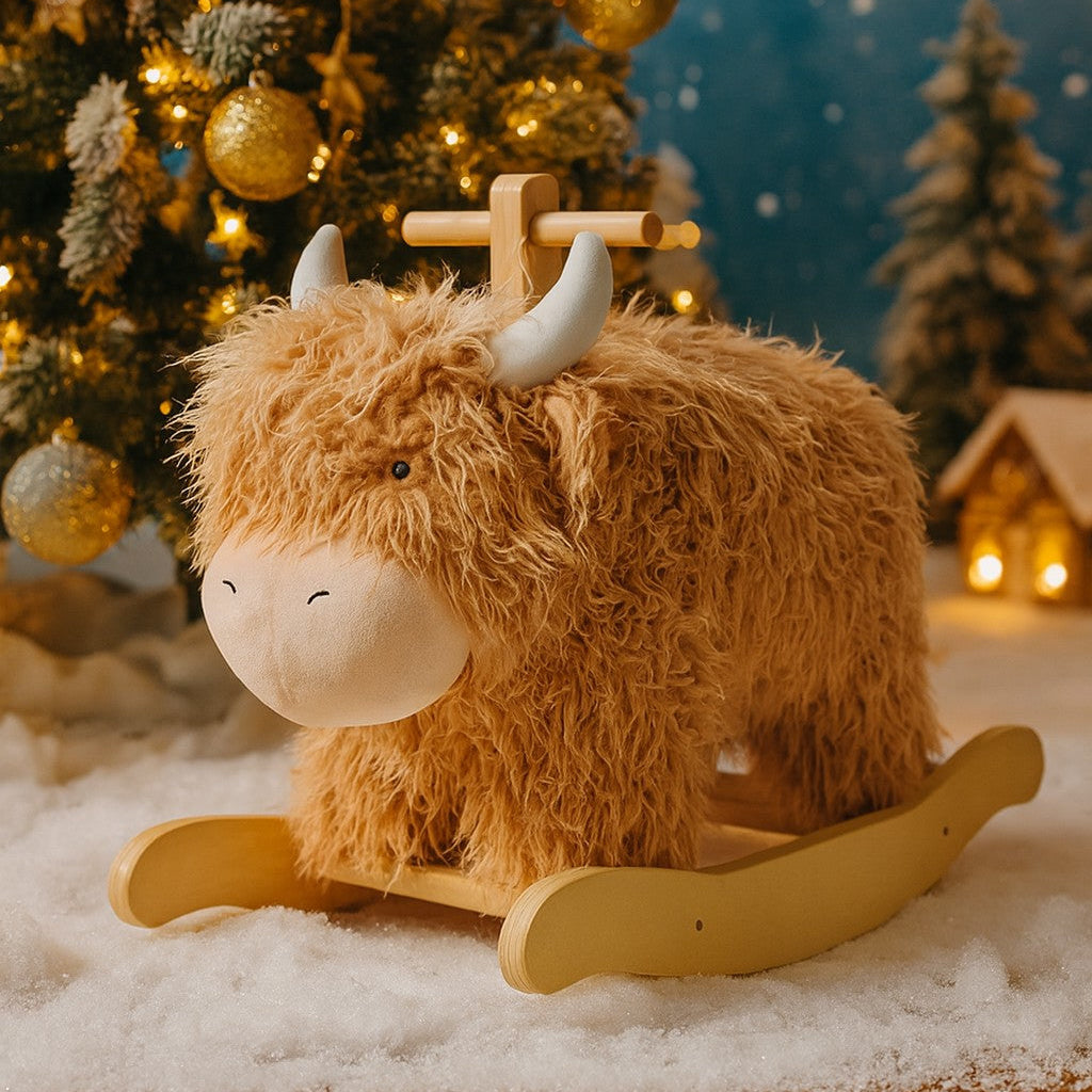Plush toy Highland cow on a wooden base in front of a decorated Christmas tree.