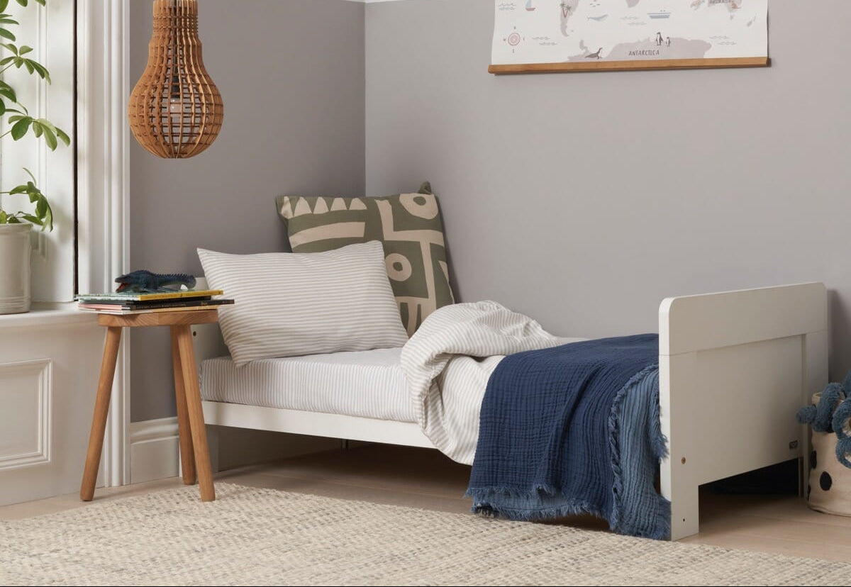 Alba cot bed in toddler bed mode in a modern nursery with cushions, wall map, and octopus teddy