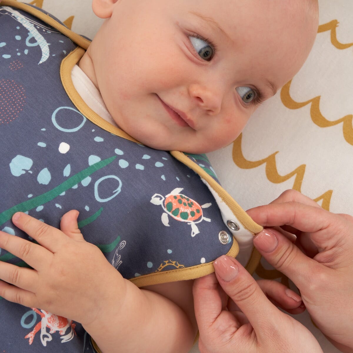 Baby wearing the Our Planet sleep bag with shoulder poppers undone, showing gentle neckline, print detail, and secure fit