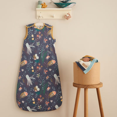 Lifestyle view of the Our Planet baby sleep bag in a nursery, styled with wooden stool and soft accessories for a cosy sleep space