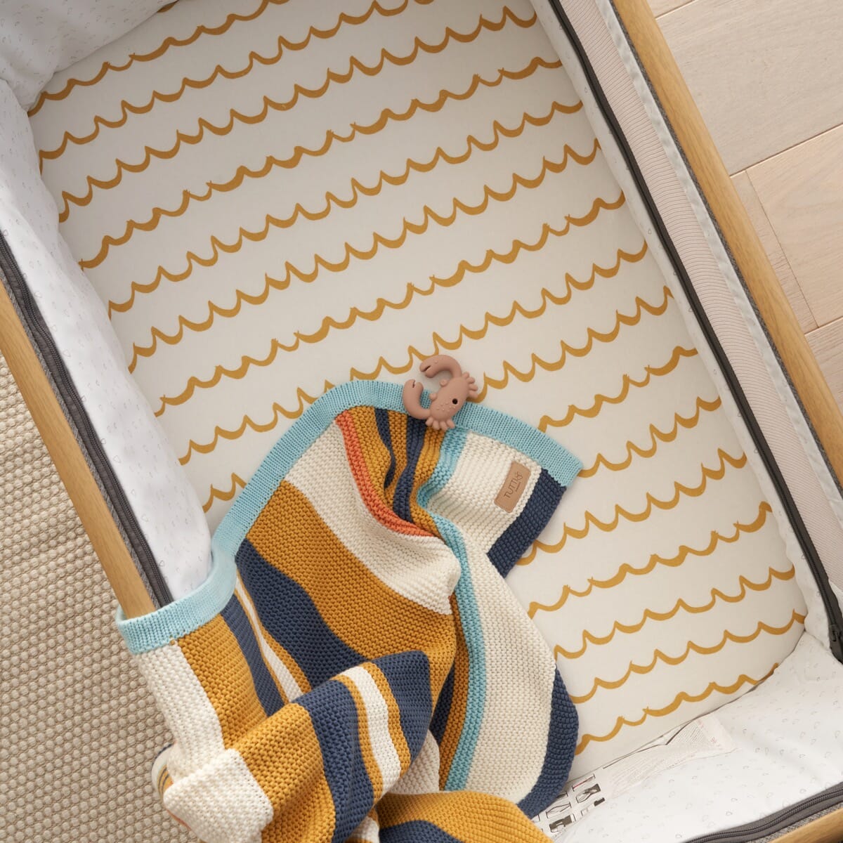 Overhead view of the CoZee bedside crib with the mustard wave our planet fitted sheet, showing its soft and snug surface for baby sleep