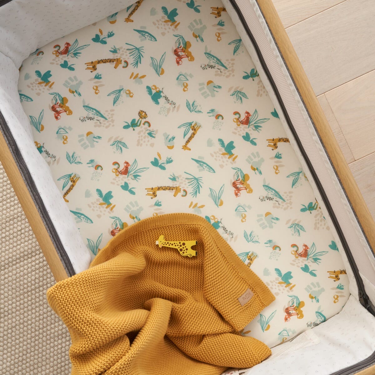 Overhead view of Run Wild bedside crib sheets in safari print, highlighting organic cotton fabric and snug fit
