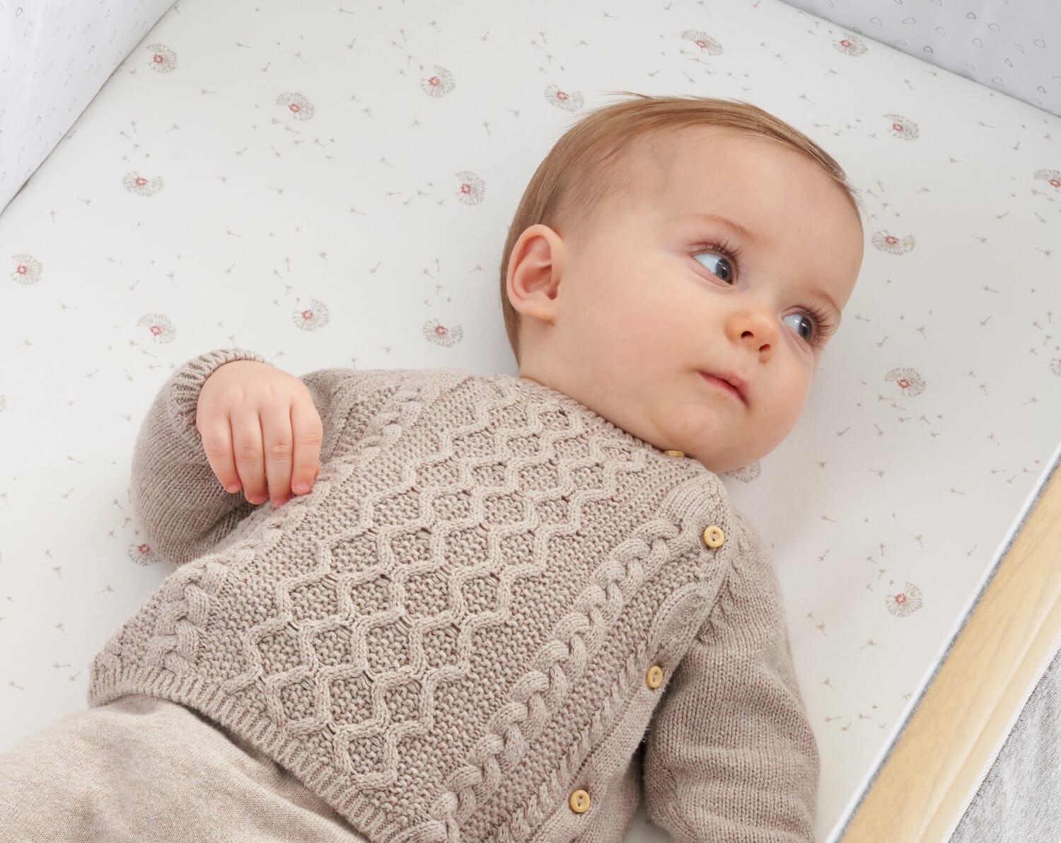 Baby lying on the Cocoon fitted sheet with soft dandelion print, showing a calm moment and the sheet’s gentle, breathable texture