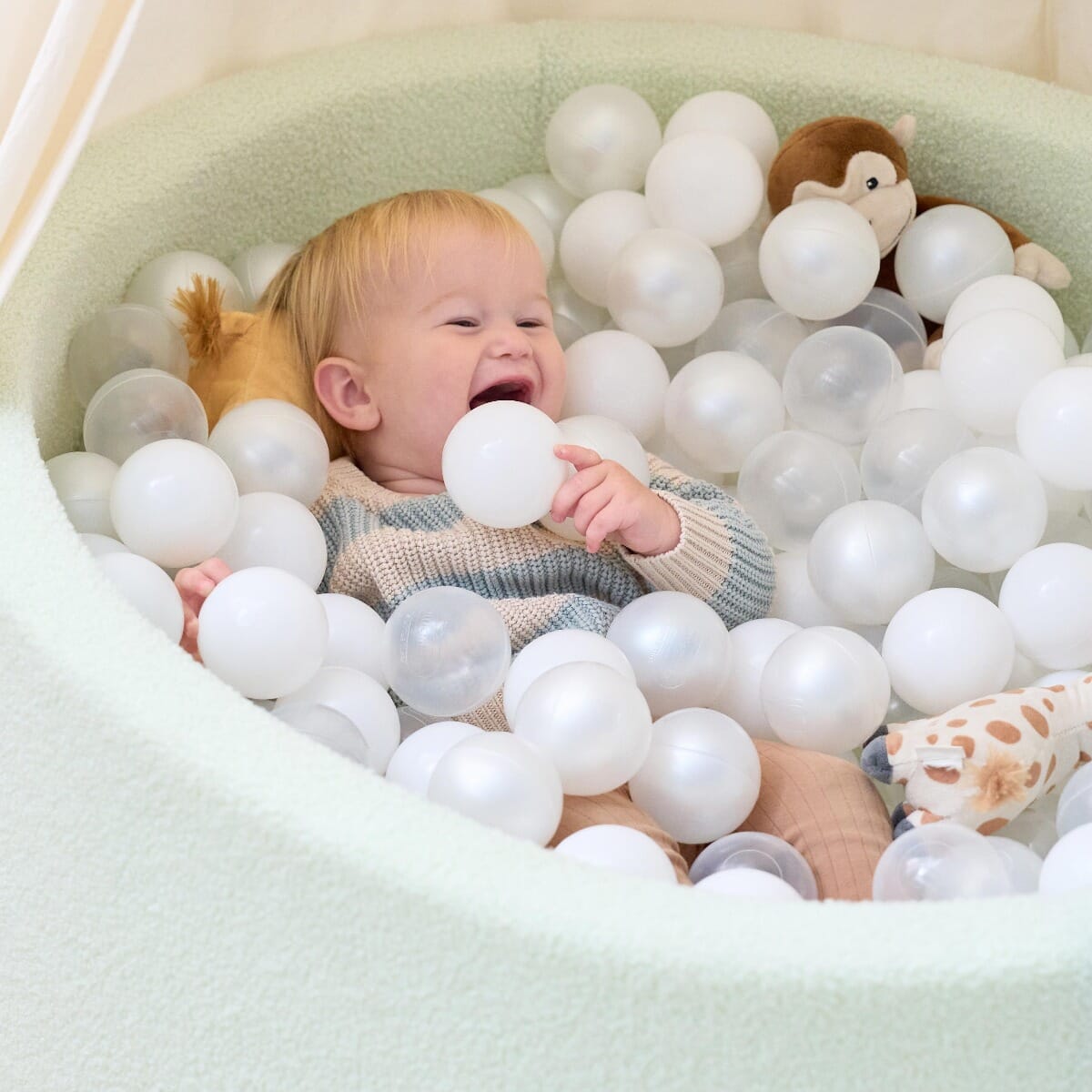 Close-up of a baby relaxing in the Bola baby ball pit in sea mist, surrounded by soft white balls for gentle sensory play