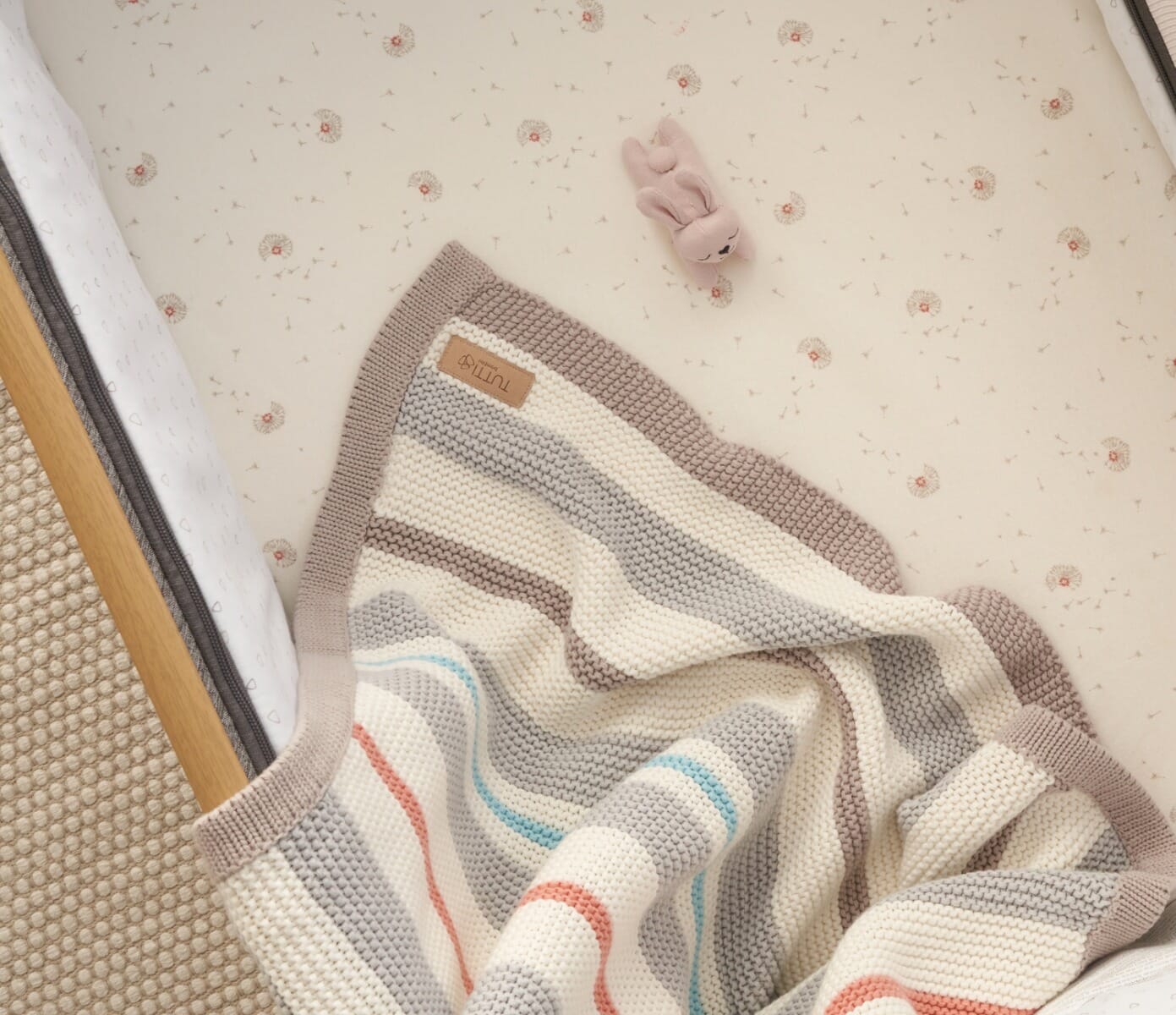 Overhead view of the Cocoon chunky knitted baby blanket styled in a cot, showcasing neutral tones and soft, tactile knit finish